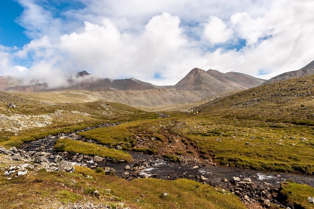 Ascenso a un puerto de montaña con un riachuelo y turistas a lo lejos Nubes sobre las cimas de las montañas Horizontal