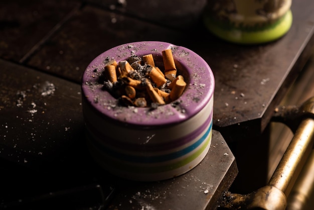 Aschenbecher mit vielen Zigarettenkippen auf dunklem Hintergrund
