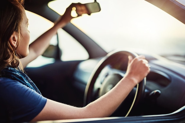 Asegurándose de tener una visión clara de su entorno Captura recortada de una mujer joven ajustando el espejo retrovisor de su automóvil