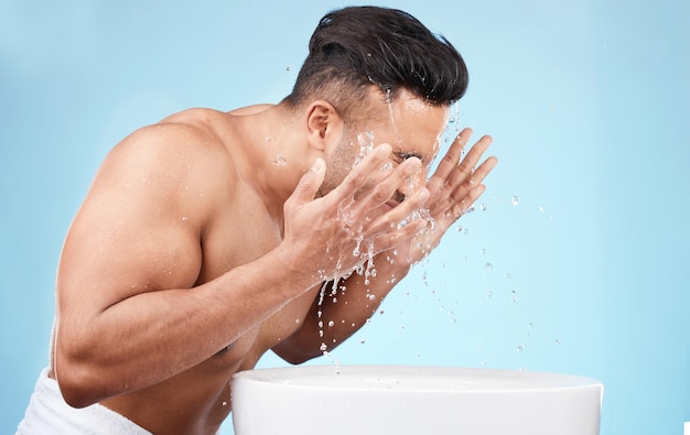 Foto aseo limpio y hombre que se lava la cara con agua para el cuidado de la piel higiene matutina y cuidado del cuerpo en un fondo de estudio azul bienestar de belleza y modelo con un toque de agua facial para la limpieza