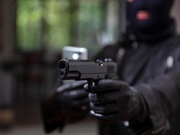 Asesino con pasamontañas sostiene móvil y pistola en mano enguantada de cuero Este es el final