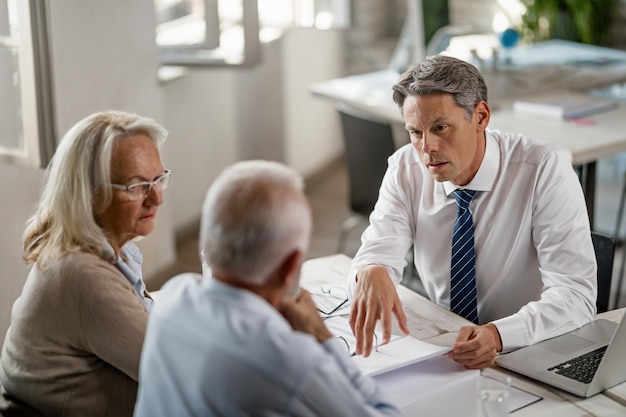 Asesor financiero discutiendo con una pareja de ancianos sobre sus informes financieros durante las consultas en la oficina