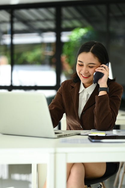 Asesora financiera femenina amigable que utiliza una computadora portátil y consulta al cliente a distancia por llamada de teléfono móvil