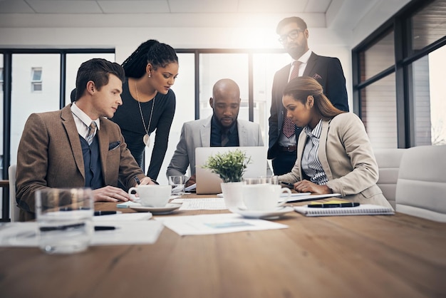 Así es como se ven nuestros competidores Foto de un grupo de jóvenes empresarios usando una computadora portátil juntos durante una reunión en una oficina moderna