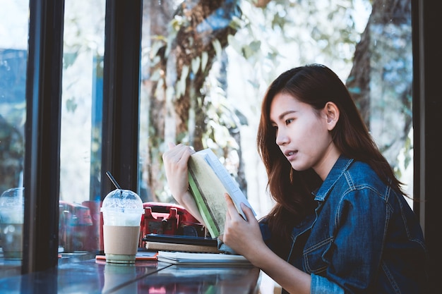 Asia adolescente sentado solo leyendo un libro en la barra de café.