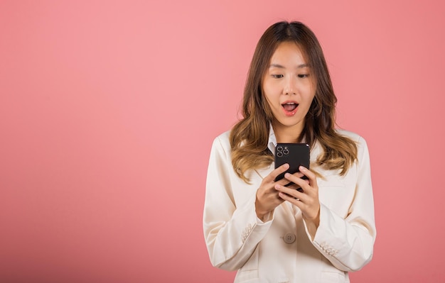 Asia feliz retrato hermosa linda mujer joven adolescente sonriendo de pie sorprendido emocionado wow gesto con teléfono móvil inteligente mirando estudio de teléfono inteligente tiro aislado fondo rosa con espacio de copia