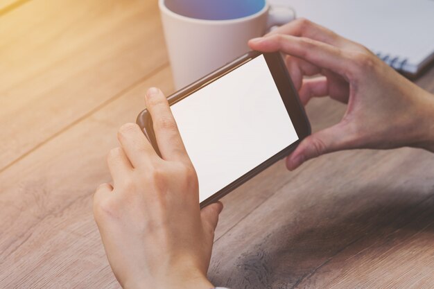 Asia-Frauenhand, die Telefon in der Kaffeestube hält und verwendet.