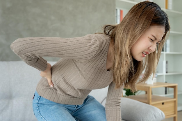 Asia hermosa mujer sosteniendo la parte inferior de la espalda mientras y sufren de dolor insoportable salud y problemas dolor crónico de espalda dolor de espalda en la oficina síndrome escoliosis hernia de disco inflamación del músculo