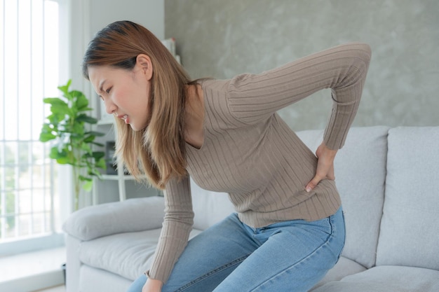 Asia hermosa mujer sosteniendo la parte inferior de la espalda mientras y sufriendo de dolor insoportable salud y problemas dolor crónico de espalda dolor de espalda en la oficina síndrome escoliosis hernia de disco inflamación del músculo