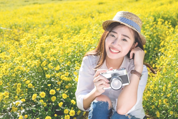 Asia hipster linda chica adolescente con la cámara en el jardín de flores de color amarillo, con el concepto de naturaleza de tono vintage