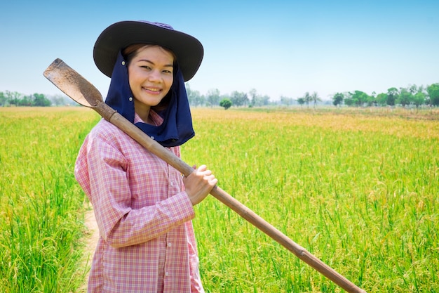 Asia joven agricultor mujer feliz sonrisa y herramienta de tenencia en un campo de arroz verde