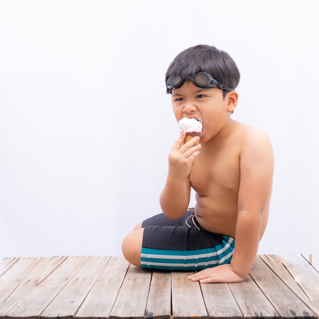 Asia lindo un niño comiendo helado y vistiendo traje de baño sobre fondo blanco,