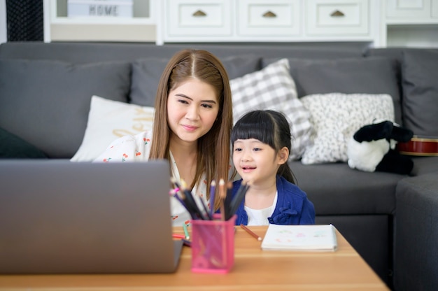 Asia mamá e hija felices están usando la computadora portátil para estudiar en línea a través de Internet en casa. Concepto de e-learning durante el tiempo de cuarentena.