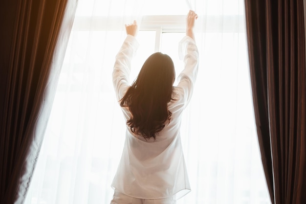 Asia mujer joven se despierta renovada por la mañana y se relaja en el dormitorio de vacaciones. Asia, asia, relajarse, solo, tecnología, concepto de estilo de vida.