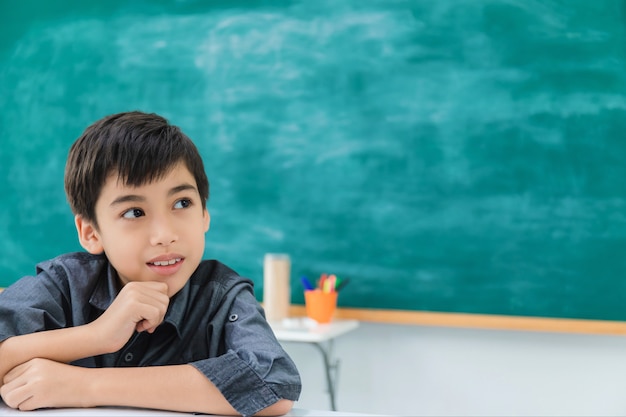 Asian feliz menino de escola sonhando e pensando no quadro negro