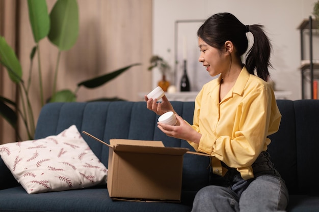 Asian Lady Holding Delivered Moisturizer Jars Caja de desembalaje en casa