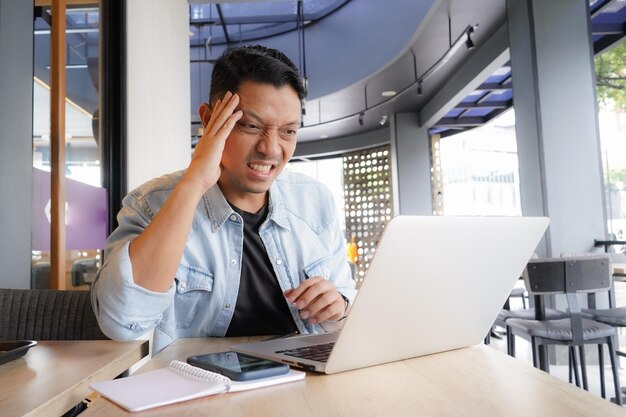 Asiater bekommt Druck, müde Kopfschmerzen, Halsschmerzen, Laptop-Mobiltelefon in einem Café.