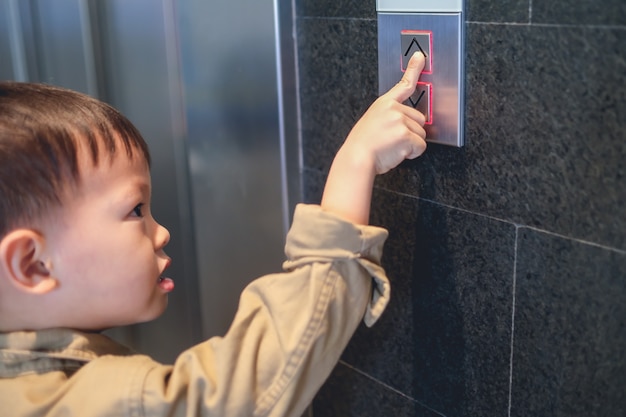 Asiático de 3 a 4 años de edad, niño pequeño niño parado frente al elevador tratando de presionar el botón elevador / elevador