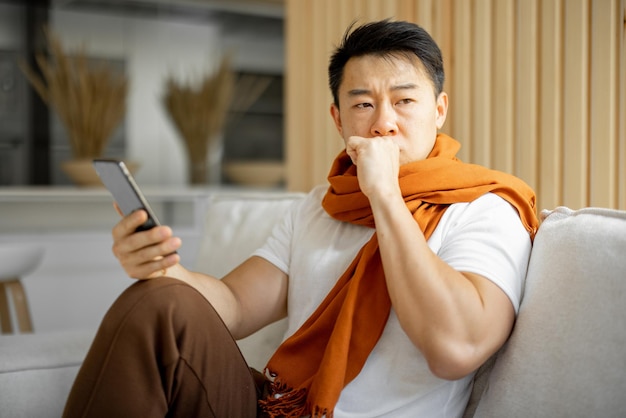 Asiático doente tossindo e usando smartphone