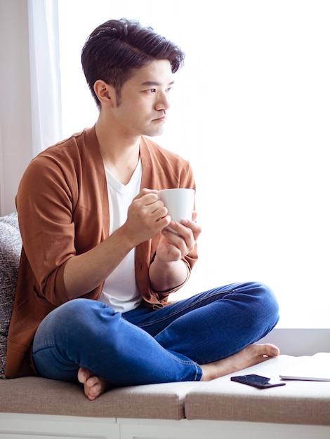 Asiático jovem bonito bebendo em casa