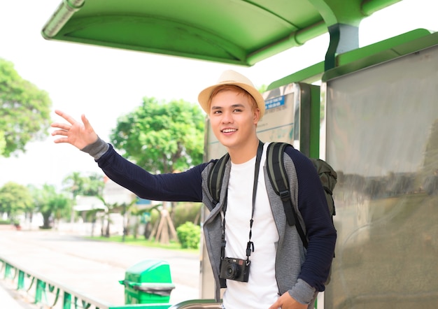 Asiático jovem bonito esperando seu ônibus e sorrindo