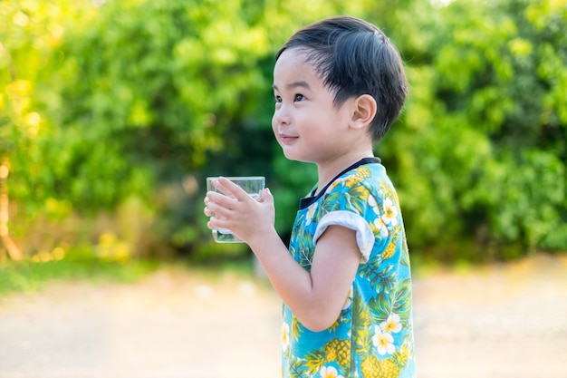 Asiático lindo sonrisa Boy agua potable para saludable y refrescante con árbol verde