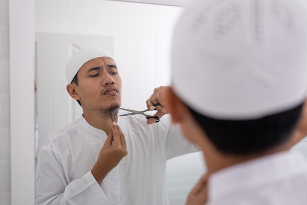 Asiático muçulmano que não tem certeza de raspar a barba com uma tesoura