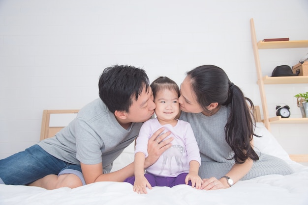 Asiático pai e mãe beijando sua filha na cama em casa