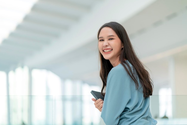 Foto asiático sorridente nômade digital feminino alegre mão segure o tablet olhe para a câmera retrato shotfelicidade sorrindo ásia mulher em pé no corredor da faculdade do escritório com atitude sorridente positiva