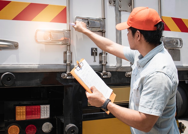 Asiático, um motorista de caminhão segurando a prancheta sua porta de aço do contêiner de carga de verificação de segurança.