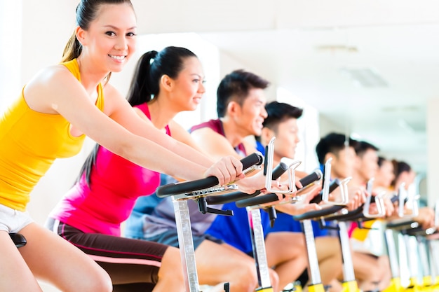 Los asiáticos en bicicleta de spinning en el gimnasio de fitness