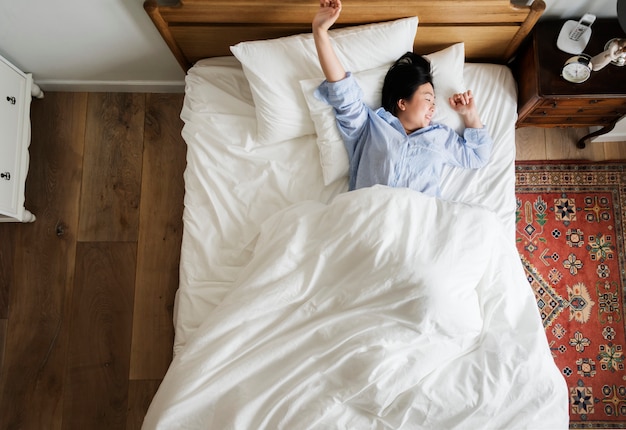 Asiatin auf dem Bett, das morgens aufwacht