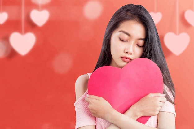 Asiatin, die ein rotes Herz mit einem traurigen Ausdruck hält. Valentinstag