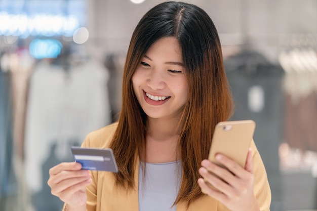 Asiatin, die Kreditkarte mit Handy für das on-line-Einkaufen im Kaufhaus verwendet