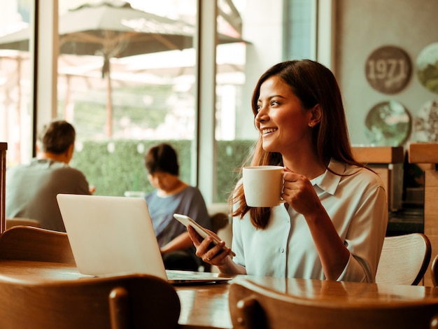 Asiatin, die mit Laptop im Kaffeeshopcafé arbeitet