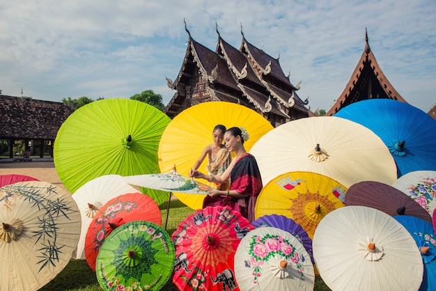 Asiatin, die traditionellen Kostümmalereiregenschirm, Lanna-Art Nord-chiangmai Thailand trägt