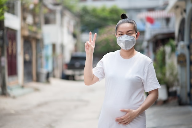 Asiatin hebt die Hände, um einen Symbolsieg zu erringen, indem sie eine Maske trägt, um PM 2,5-Staub und Koronavirus zu verhindern, Covid 19