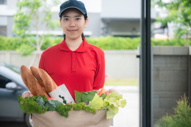 Asiatin liefern Frau Handling Tasche von Lebensmitteln, geben Sie dem Kunden vor dem Haus