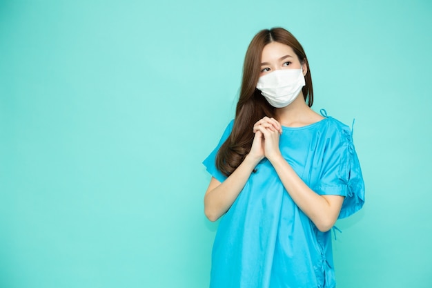 Asiatin Patientenanzug mit weißer Gesichtsmaske isoliert auf grünem Studiohintergrund