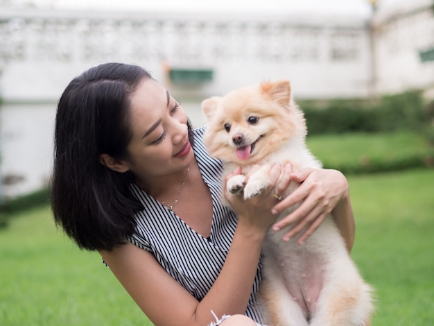 Asiatin spielt mit ihrem pomeranian Welpen im Garten.