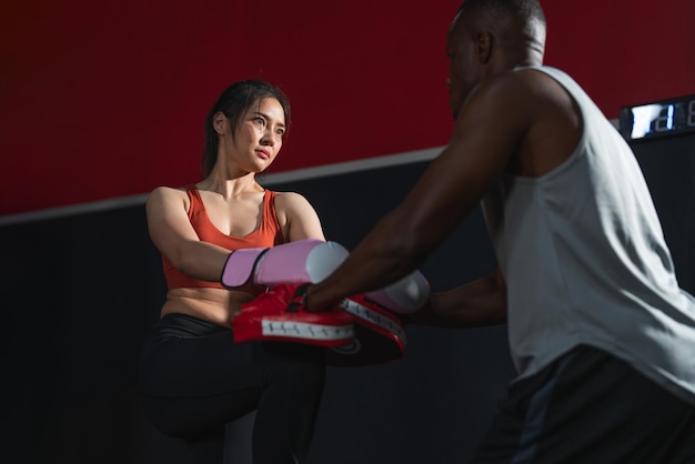 Asiatin trägt Boxhandschuhe beim Boxtraining mit Manntrainer im Fitnessstudio