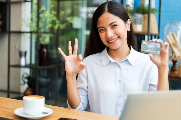 Asiatin, welche die Kreditkarte online kauft im Kaffeestubecafé verwendet