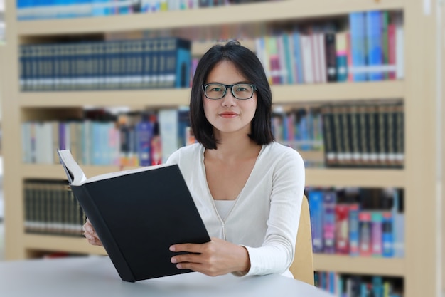 Asiatinlesebuch mit Lächeln und in der Bibliothek gerade schauen.