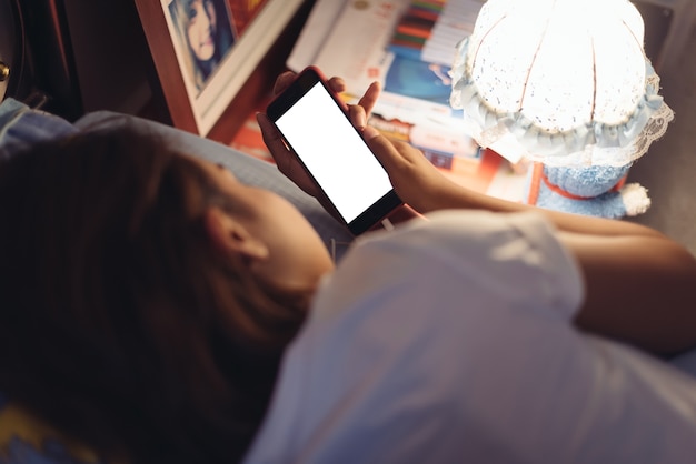 Asiatinnen, die das intelligente Telefon auf dem Bett verwenden, bevor sie nachts schläft.