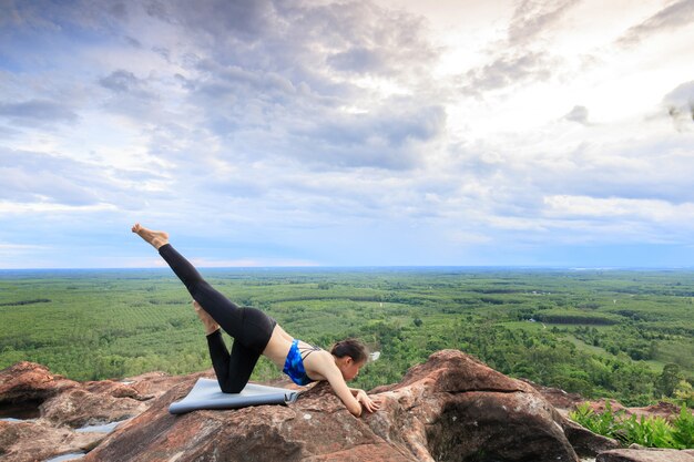 Asiatinnen spielen es Yoga auf der Gebirgsfelsenklippe.