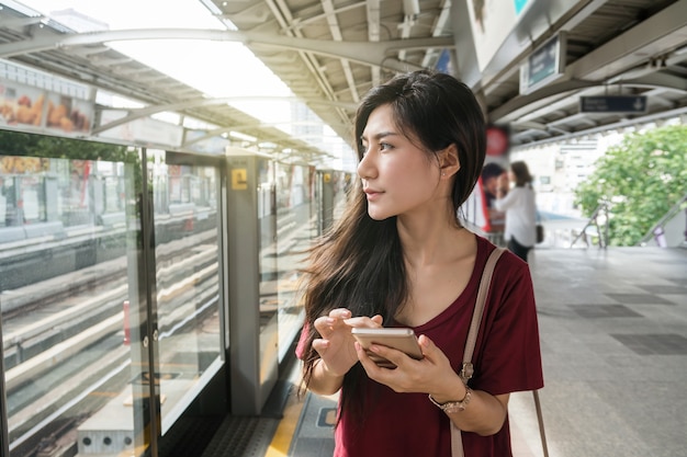 Asiatinpassagier mit der zufälligen Klage unter Verwendung des intelligenten Handys in den Schienen BTS Skytrain oder MRT