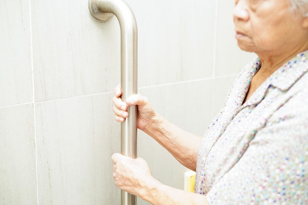 Asiatische ältere alte Patientin benutzt Toilettenstützschiene im Badezimmer Handlauf Sicherheit Haltegriff Sicherheit im Pflegekrankenhaus