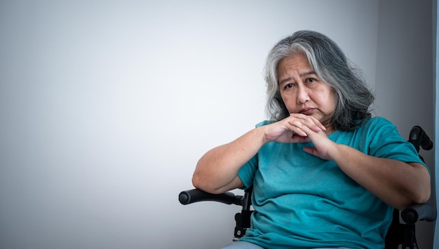 Asiatische ältere Frau, die im Rollstuhl sitzt, ist traurig und ängstlich von ihrer eigenen Krankheit