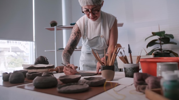 Foto asiatische ältere frau, die zu hause töpferarbeiten genießt eine keramikerin stellt in einem studio neue töpferwaren her