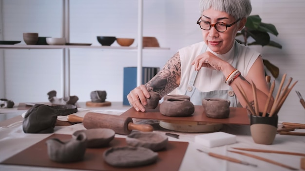 Asiatische ältere Frau, die zu Hause Töpferarbeiten genießt Eine Keramikerin stellt in einem Studio neue Töpferwaren her